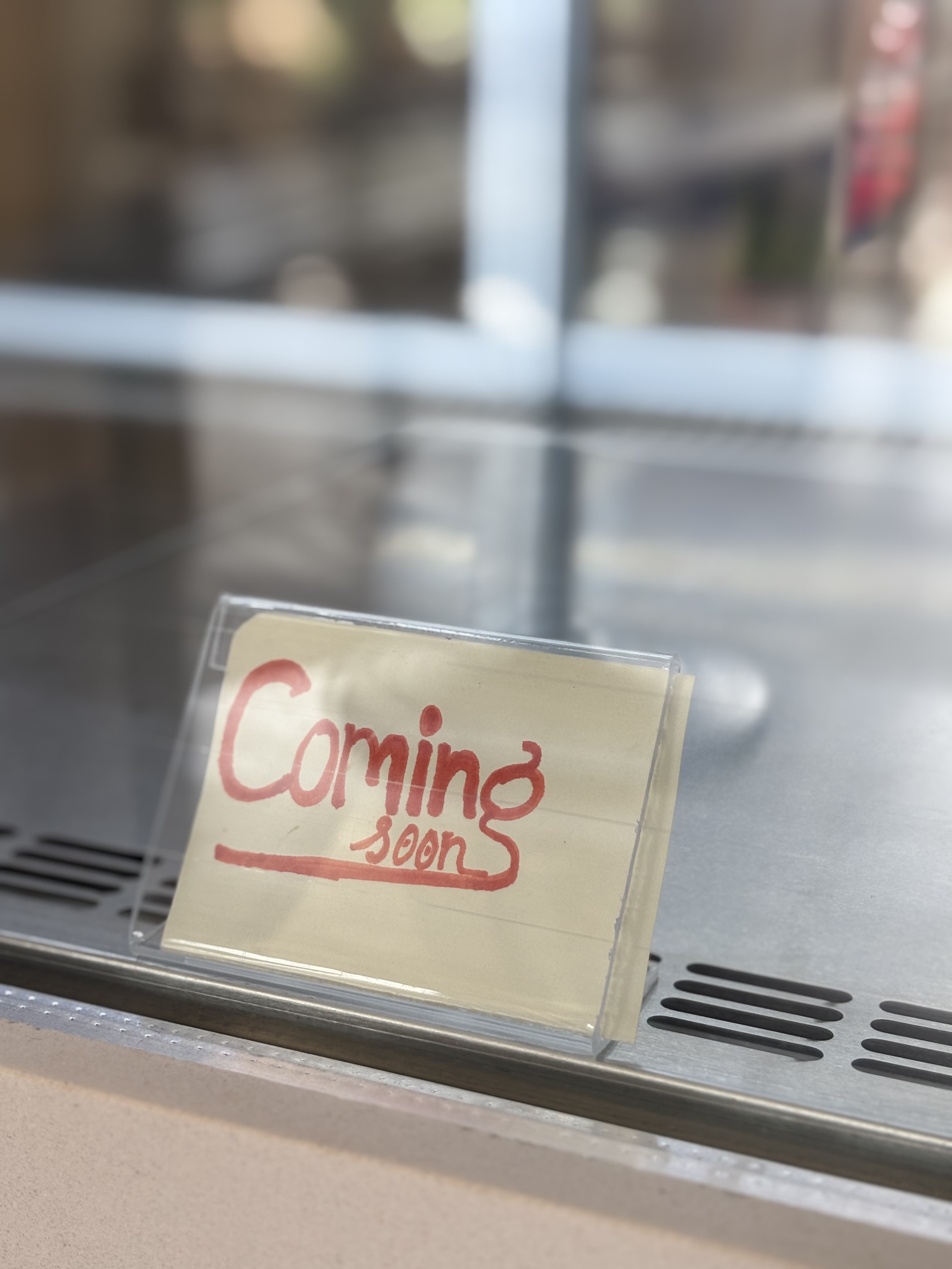 A sign that reads "Coming soon" in red ink on a yellow piece of paper is displayed inside a glass enclosure.