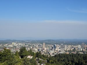 Scenic view of downtown Portland city skyline surrounded by trees and distant hills, taken from the Pittock Mansion in the evening. 