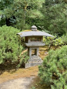 A Japanese stone lantern is placed among green pine trees and moss-covered ground. Photo taken at Portland Japanese Garden, Oregon, USA. 