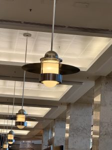 A row of hanging ceiling lamps with black shades and round bulbs, lining a corridor with marble columns. Photo taken at Seattle International Airport.