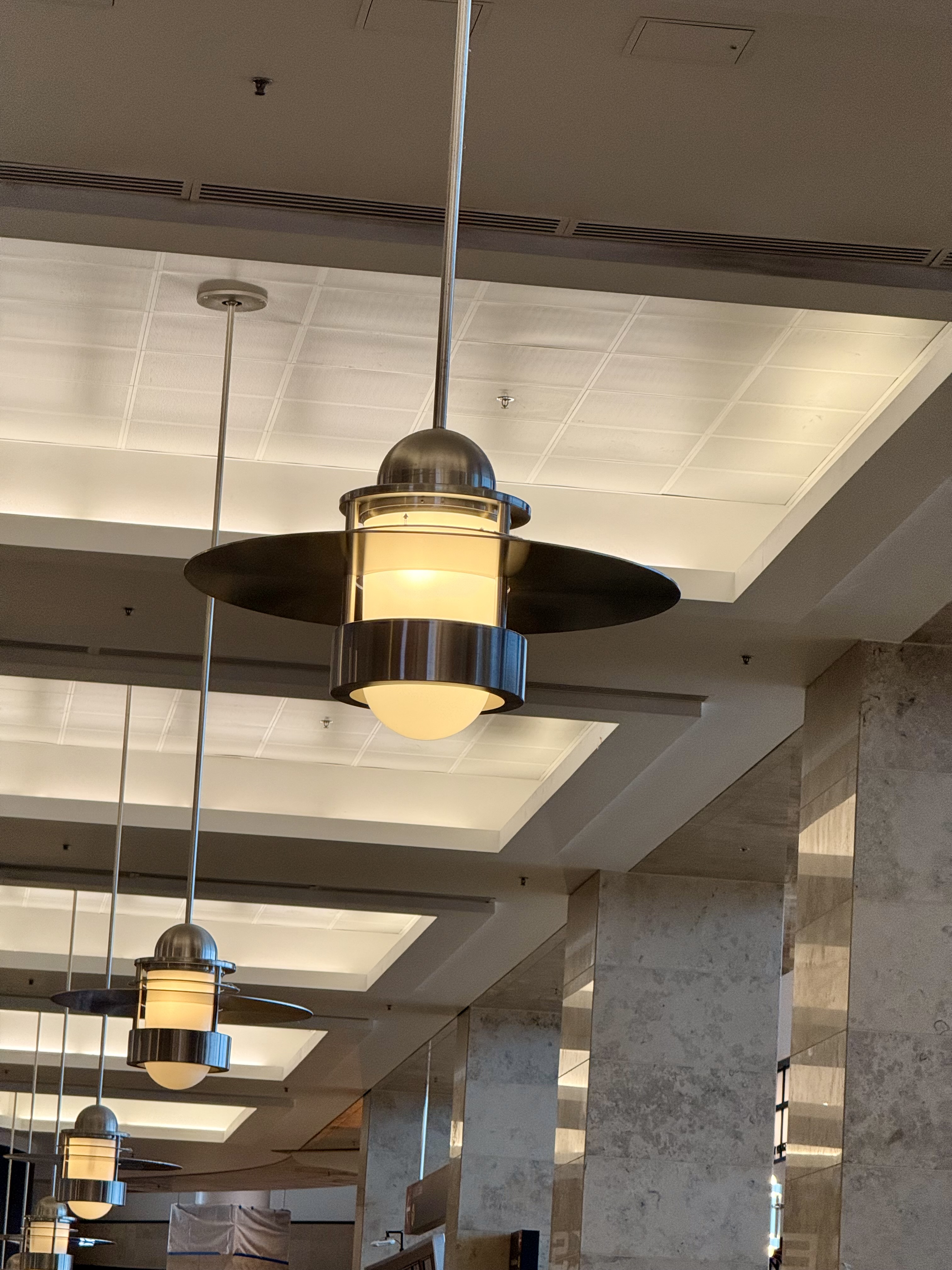 A row of hanging ceiling lamps with black shades and round bulbs, lining a corridor with marble columns. Photo taken at Seattle International Airport.