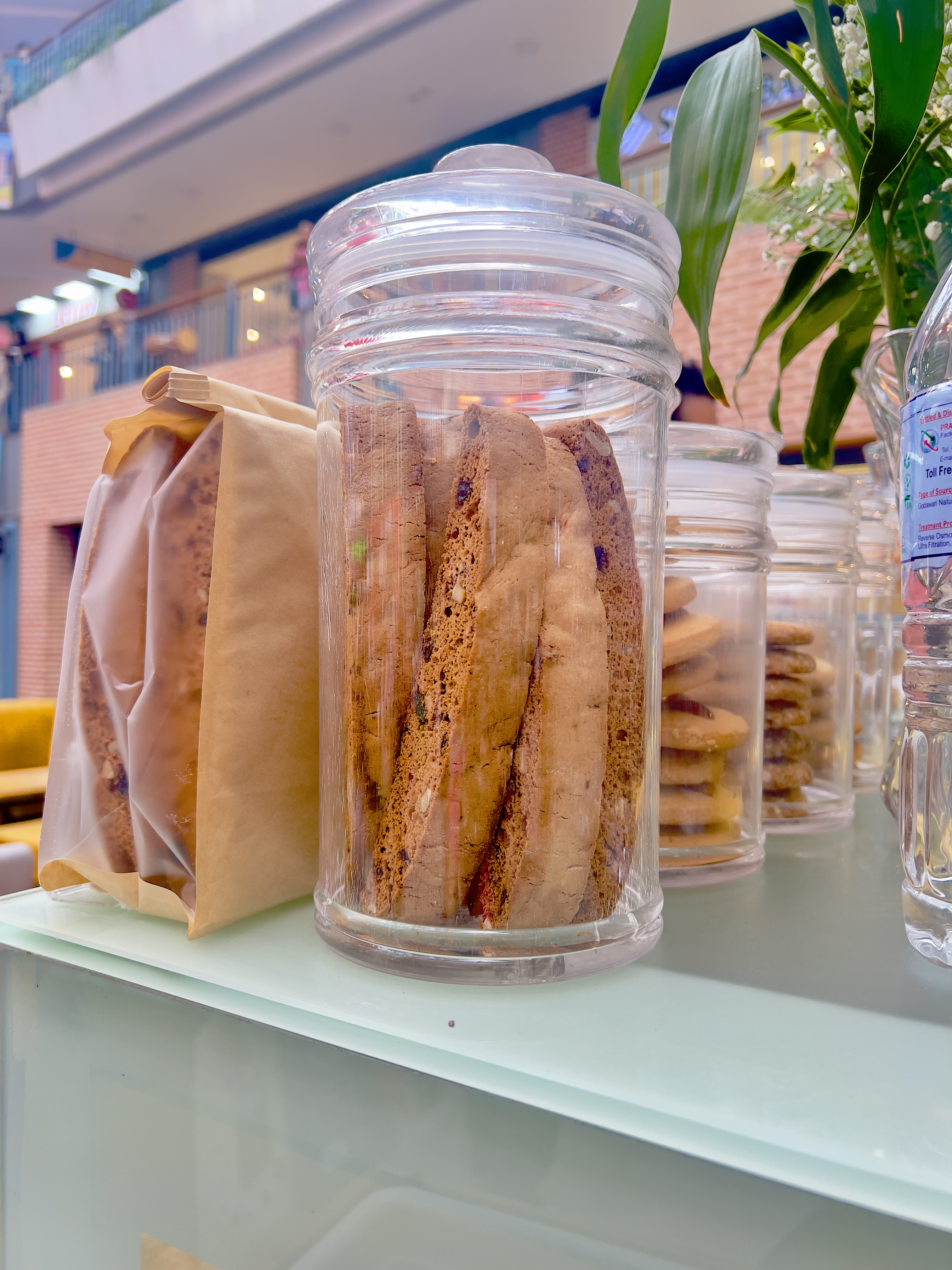 Clear jars of biscotti and cookies are displayed on a white countertop.