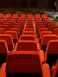 Multiple rows of empty, red seats are pictured in a movie theater.