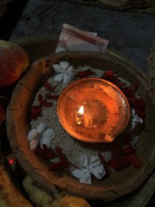 A small clay diya (oil lamp) with an orange flame is positioned in a round bowl filled with white rice.