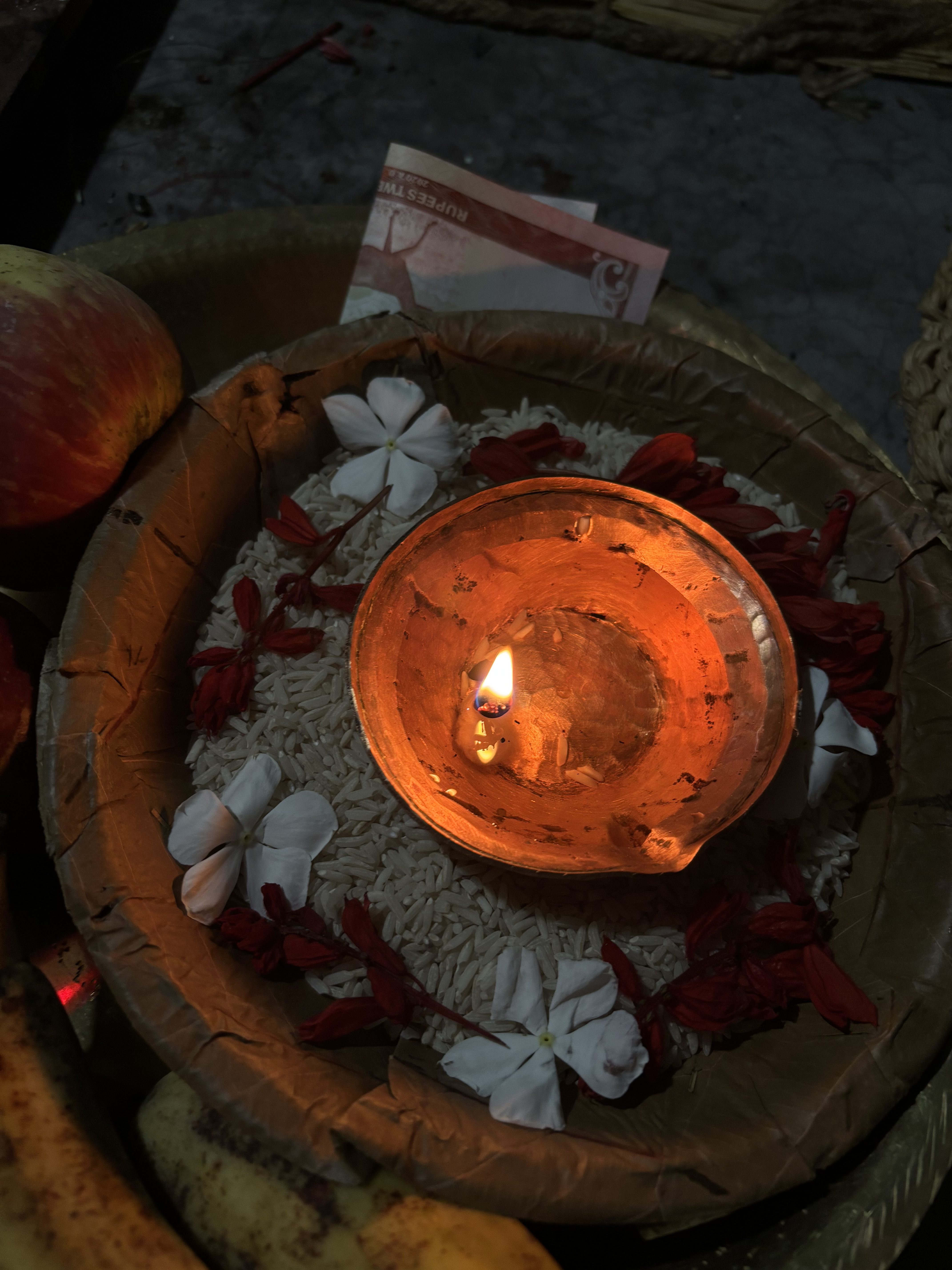 A small clay diya (oil lamp) with an orange flame is positioned in a round bowl filled with white rice.