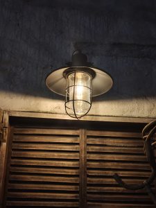 A vintage metal lamp glows above a wooden shuttered window in a dim room.
