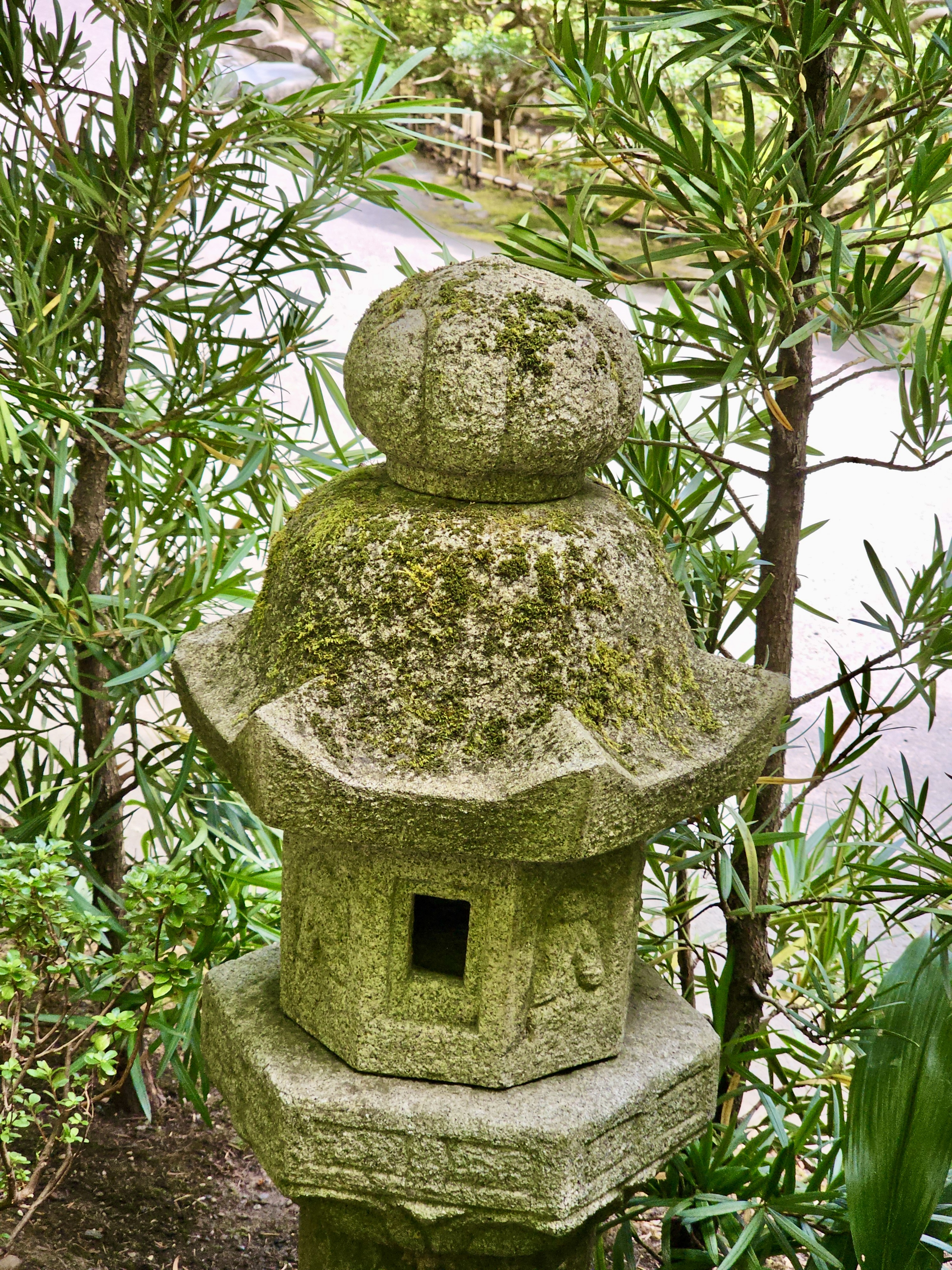 A dome-topped stone lantern stands near a path, surrounded by bamboo and leafy plants in Portland Japanese Garden.