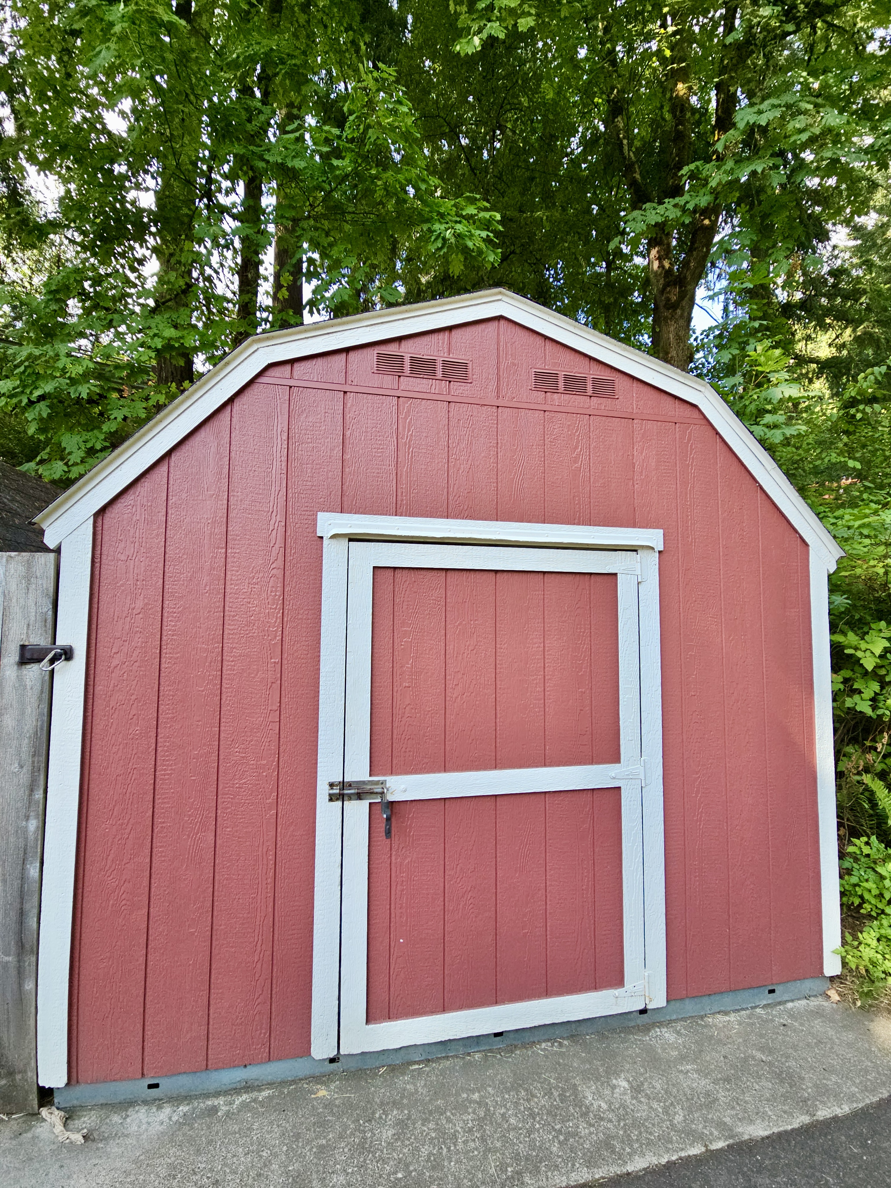 A small, red wooden shed with white trim stands beneath tall, green trees, creating a rustic look. Captured at the Oregon Zoo, Portland.
