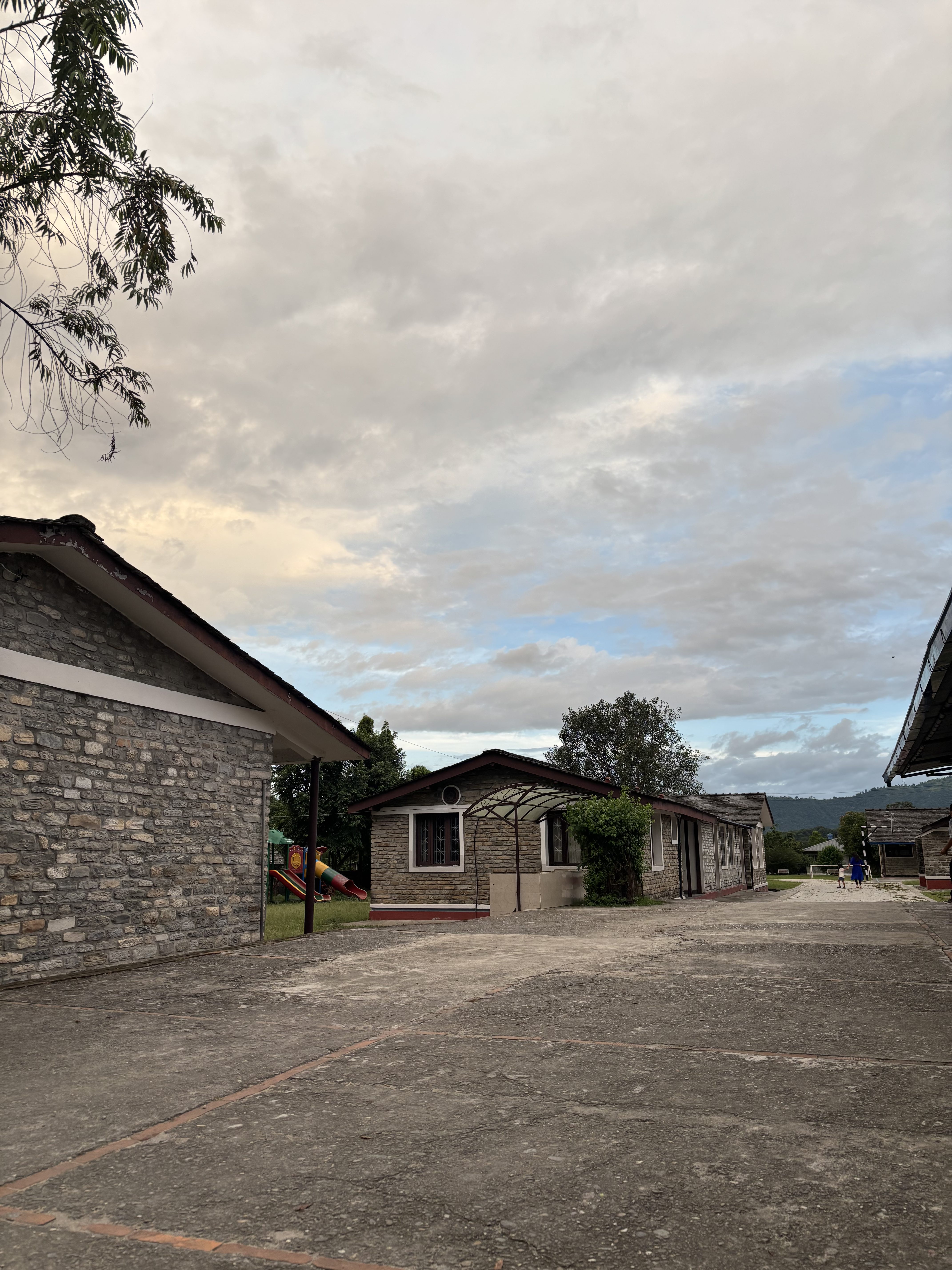 A view of a pathway leading through a small residential area featuring stone buildings with red accents
