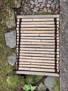 A close-up of a bamboo mat drain framed by moss and stones, used in traditional Japanese landscaping at the Portland Japanese Garden. 