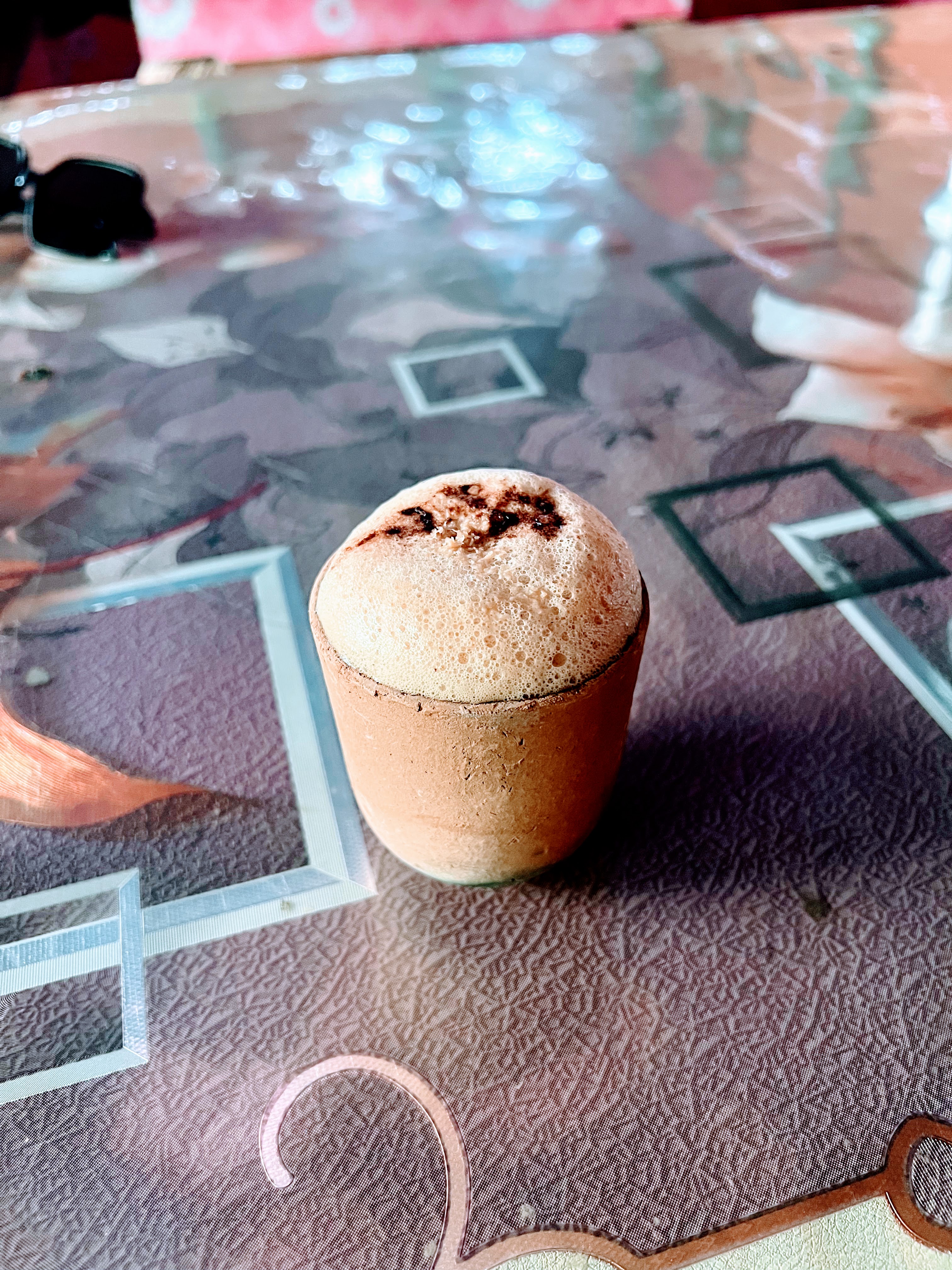 A frothy drink in a small terracotta cup known as Matka Tea, rests on a patterned table.