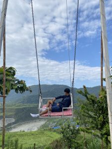 A person sits on a swing suspended high above a scenic landscape. 
