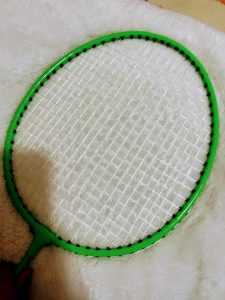  A bright green badminton racket with white strings rests on a fluffy white surface.