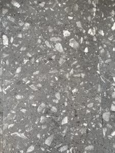 A close-up view of a polished gray terrazzo flooring, featuring a mixture of light and dark stones embedded in a smooth gray base.