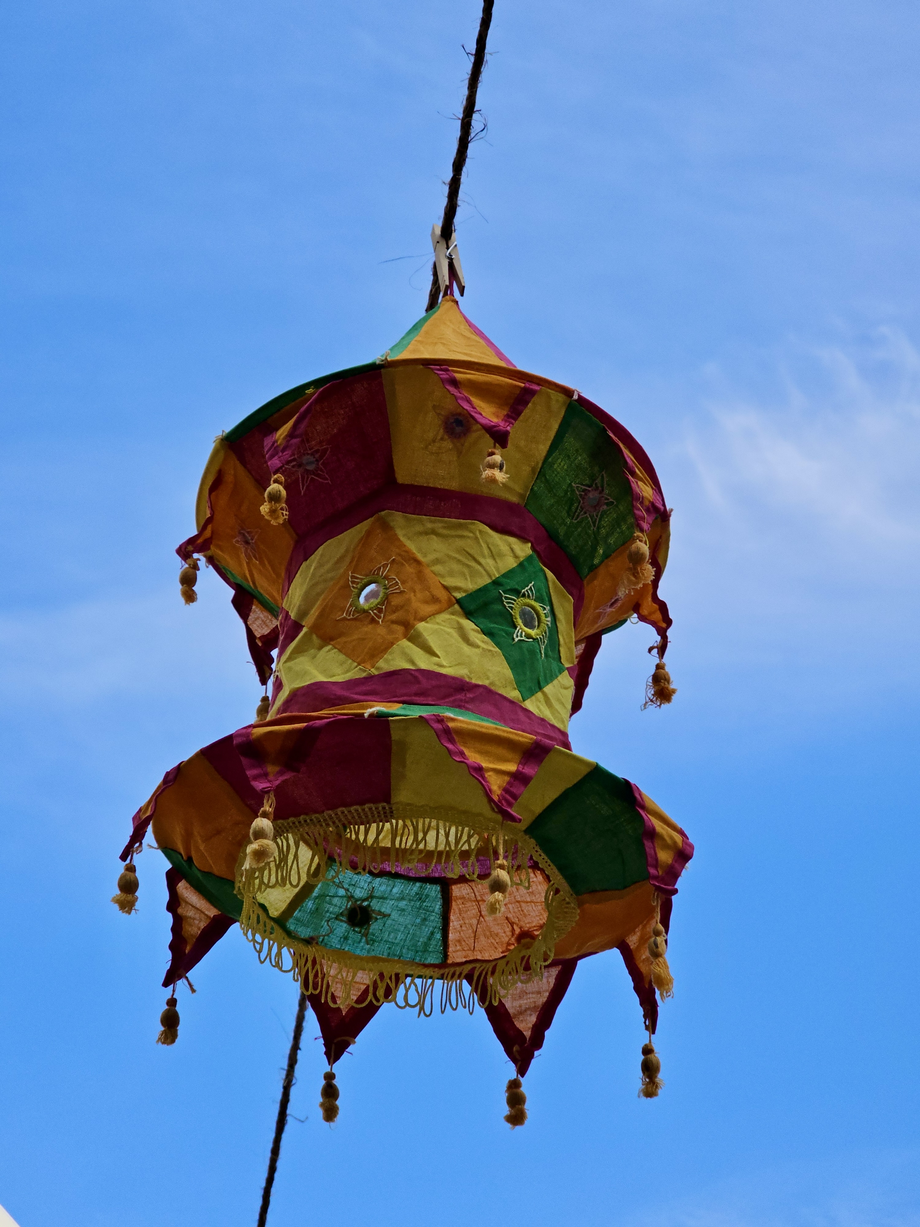 Bright and vibrant multicolor fabric lantern with tassels and mirrorwork, hanging high against a clear blue sky, captured from an Indian festival in downtown Portland, Oregon. 