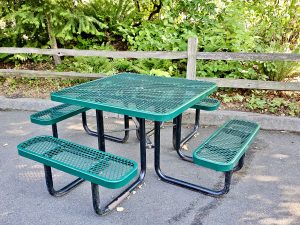 A green picnic table with four seats, placed in a quiet spot under trees near a wooden fence at the Oregon Zoo, Portland.