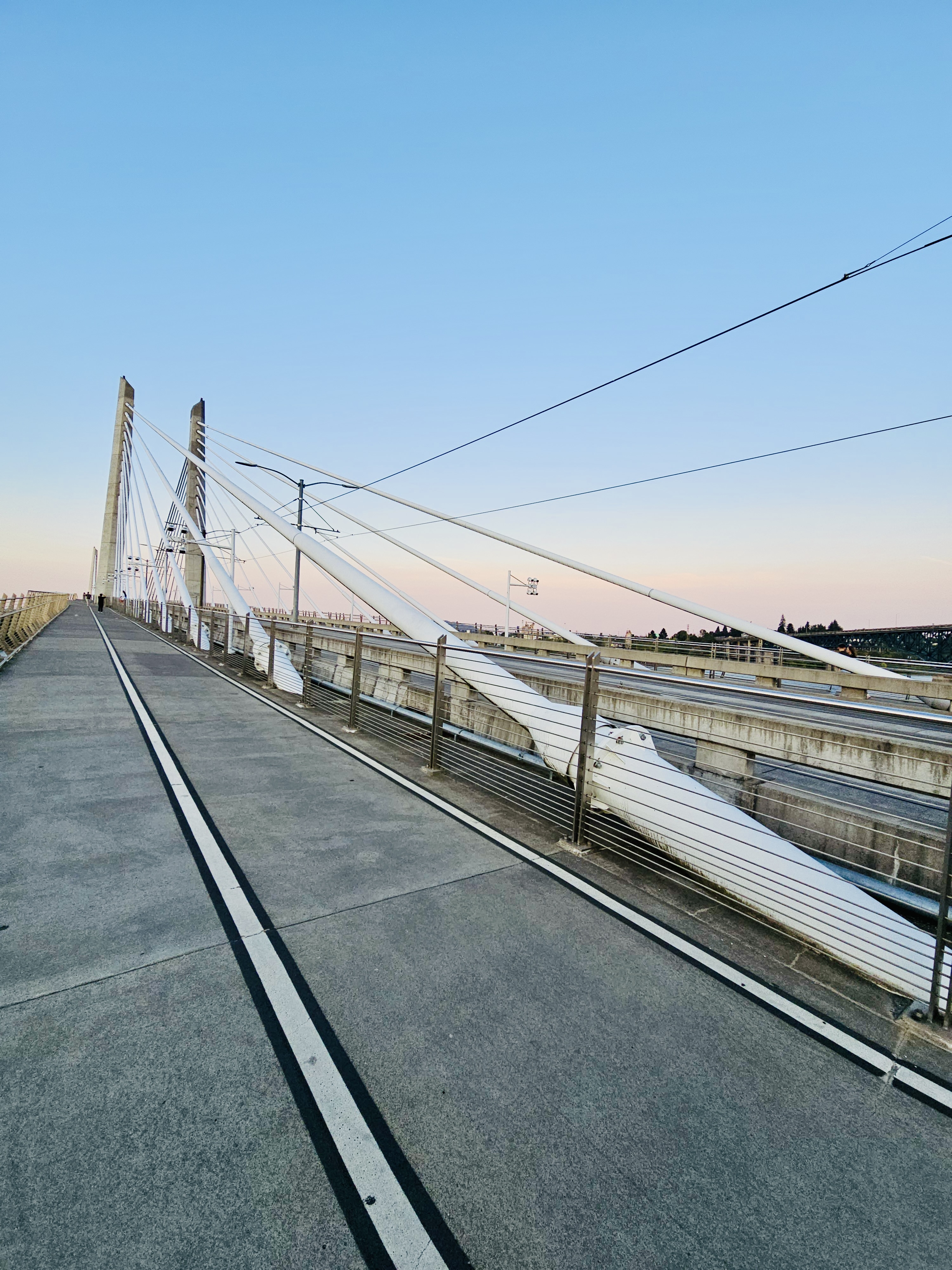 A wide pedestrian and cycle path on Tilikum Crossing Bridge in Portland, Oregon, during sunset. Shows the bridge cables, tracks, and the open sky. 