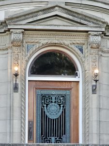 A detailed photo of an elegant wooden door with carved stone decorations and blue ironwork at Pittock Mansion, Portland, taken in the evening light.