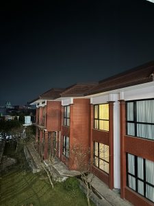 A nighttime view of a modern building made of red brick, featuring large windows with white curtains. 