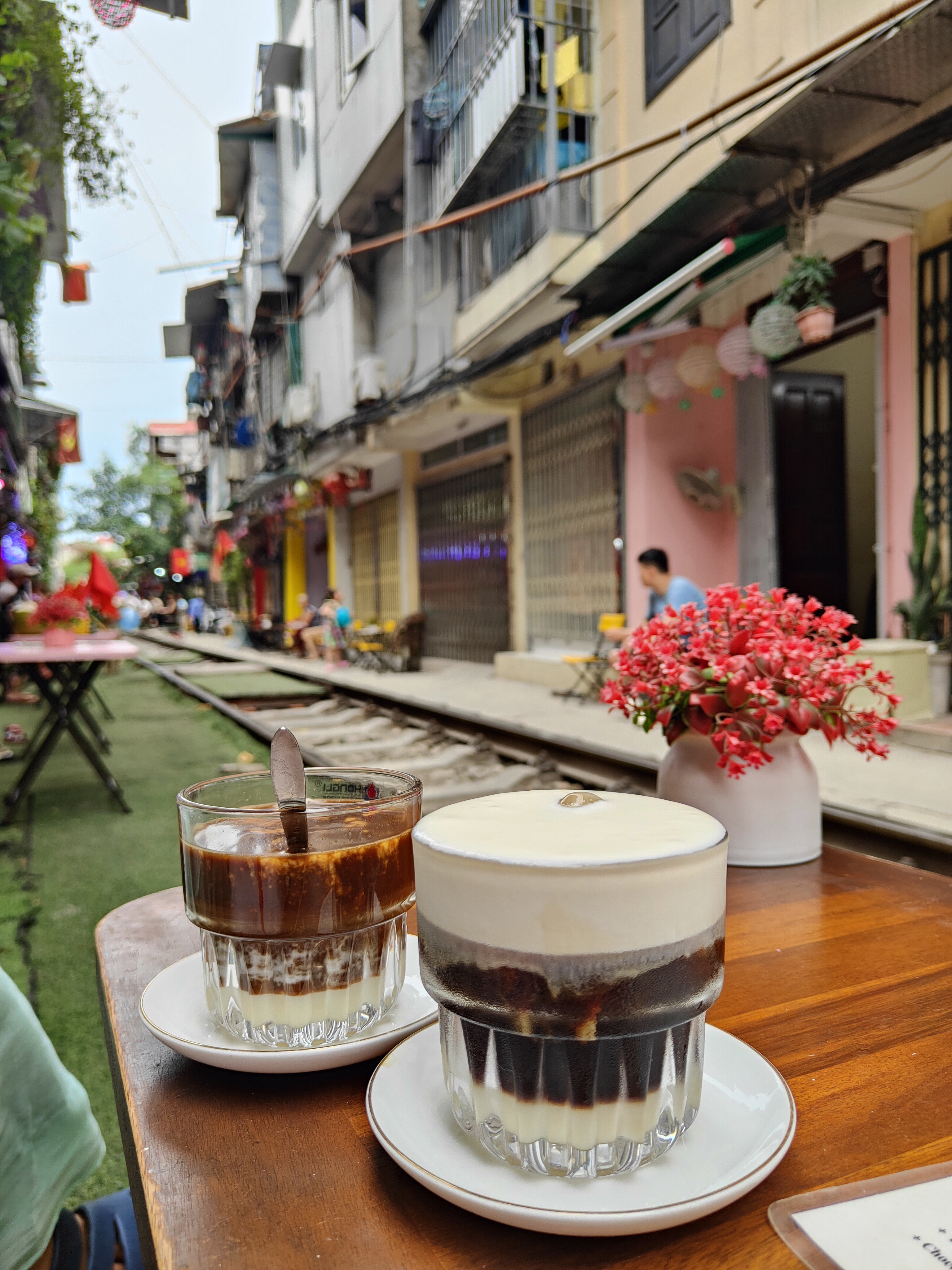 Two glasses of Vietnamese coffee sit on a wooden table along Hanoi’s Train Street — one creamy coconut, the other salt