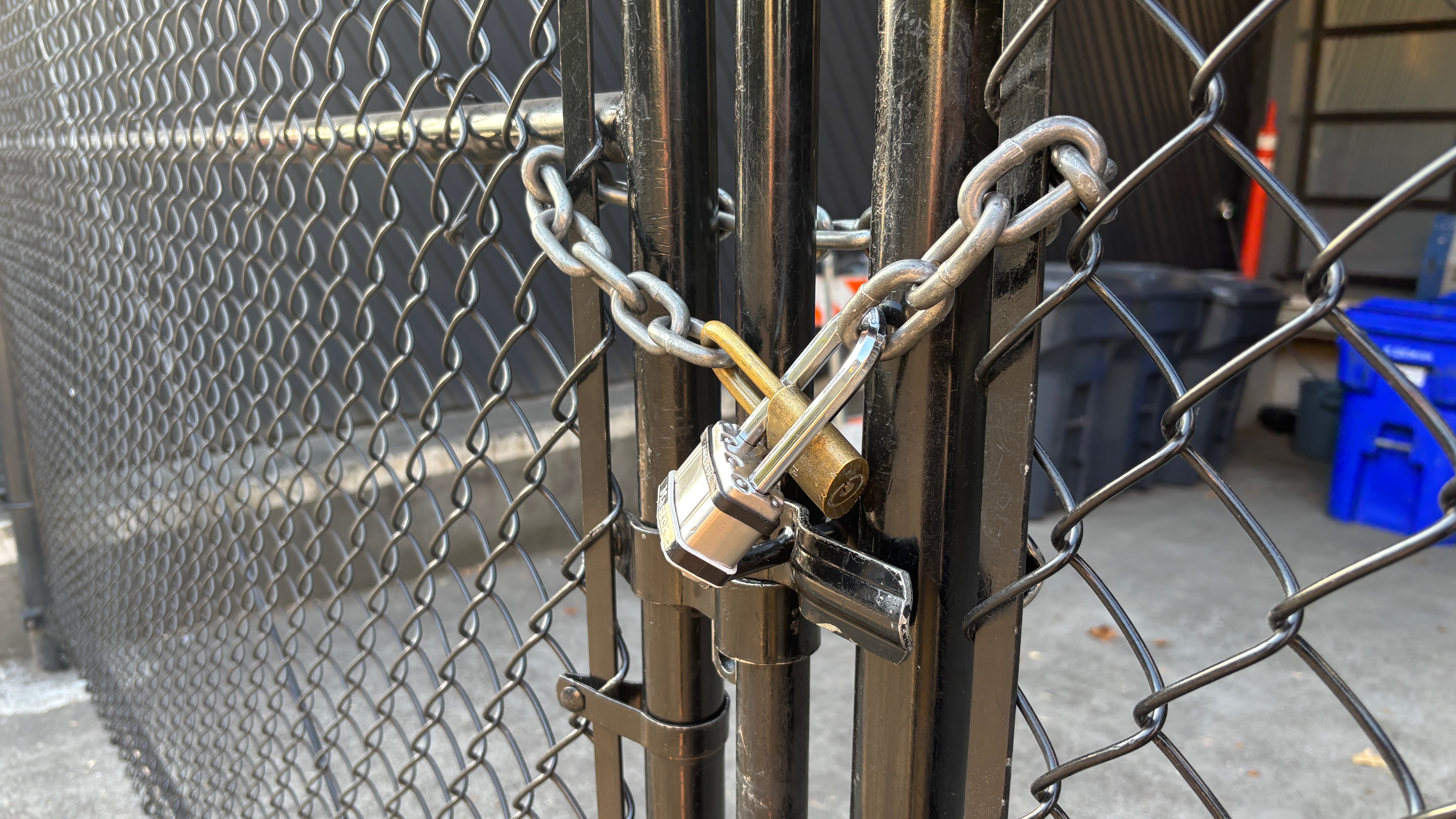A closeup of the gateway between two fences.  A chain is wrapped around the latch and it's locked with two padlocks.