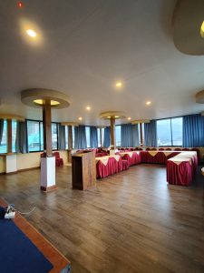 A spacious room with wooden flooring and large windows showing a scenic view.