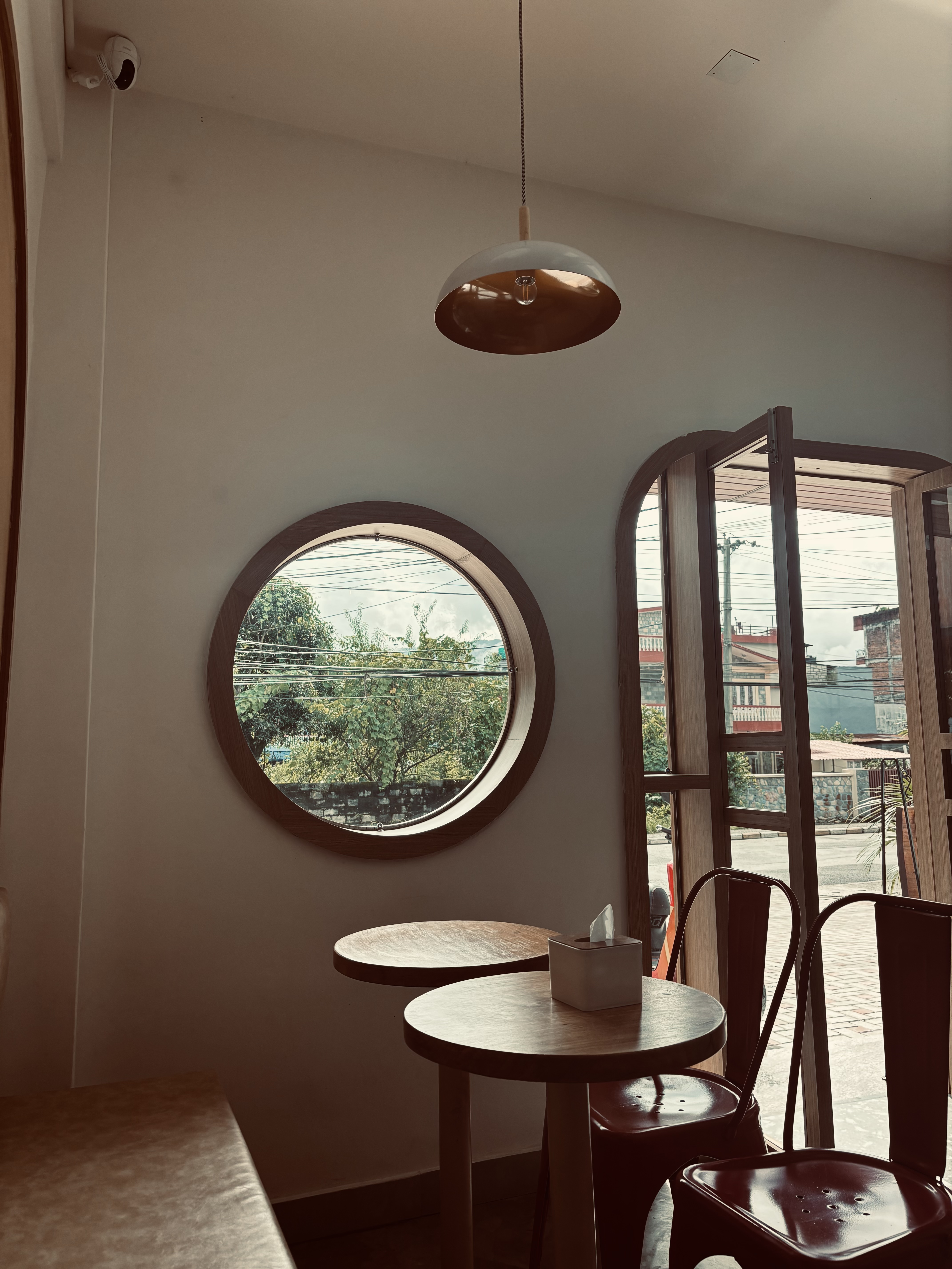 A cozy interior of a café featuring a round window with a view of greenery outside. 