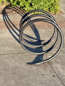A black spiral-shaped bike rack casting a long shadow on the sidewalk near Tilikum Crossing Bridge in Portland. 