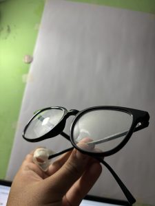 A person is holding a pair of black-framed eyeglasses with clear lenses. 