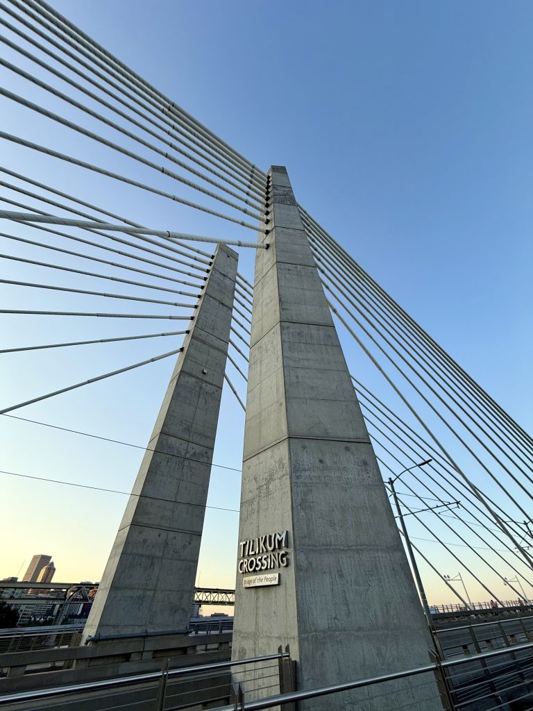 Concrete support towers and suspension cables of the Tilikum Crossing Bridge in Portland. The bridge sign reads “Tilikum Crossing – Bridge of the People.”