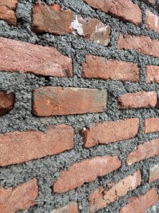 A close-up view of a brick wall under construction, featuring textured red bricks interspersed with gray mortar.