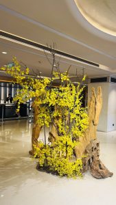 A striking decorative arrangement featuring a centerpiece made of twisted, natural wood, intertwined with bright yellow flowers.