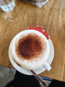 A coffee cup filled with foam on top, and covered in a brown powder.  Seen from above.
