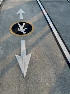 Close-up of a pedestrian direction symbol on the walking path of Tilikum Crossing Bridge, Portland. White arrows and a figure mark the lane. 