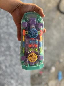 A hand holds a colorful, transparent toy car that features various components like gears and spinners.