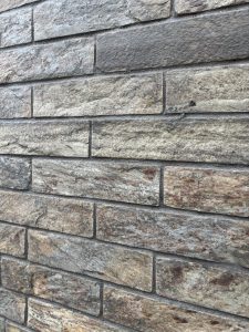 A close-up view of a textured wall made of rectangular stone bricks in shades of gray and brown, with visible variations in color and surface.