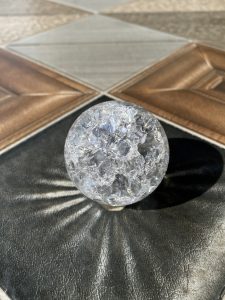 A clear, textured Crystal ball sits on a patterned surface with various shades of brown, gray, and black. 