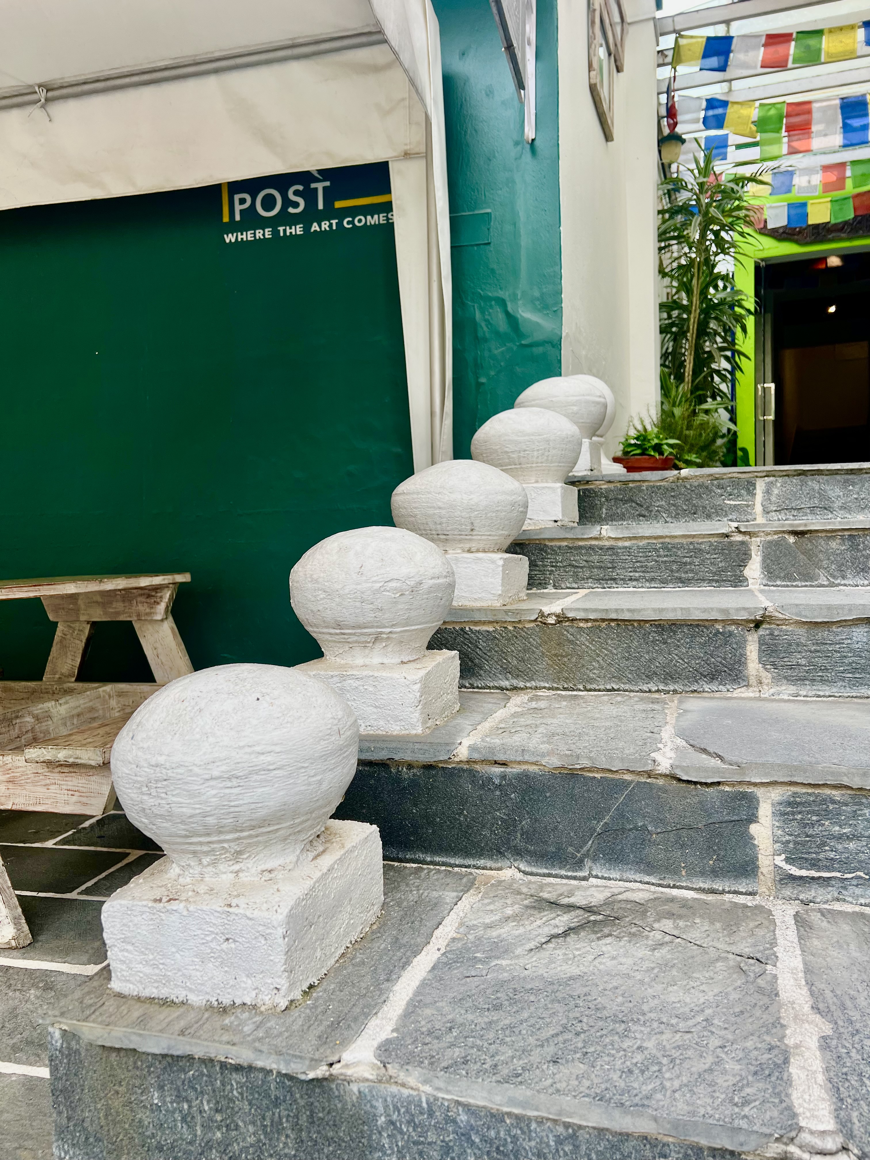 A close-up of a stone staircase with white spherical balusters leading up to a green wall with the text "POST WHERE THE ART COMES."