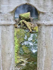 A view through a stone arch showing a small waterfall and mossy rocks in the creek below. Captured in the Columbia River Gorge National Scenic Area, Oregon. 