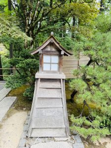 A full view of a wooden lantern with a mossy roof, placed among small trees and stone paths in the Japanese Garden, Portland. It reflects peaceful Japanese design. 