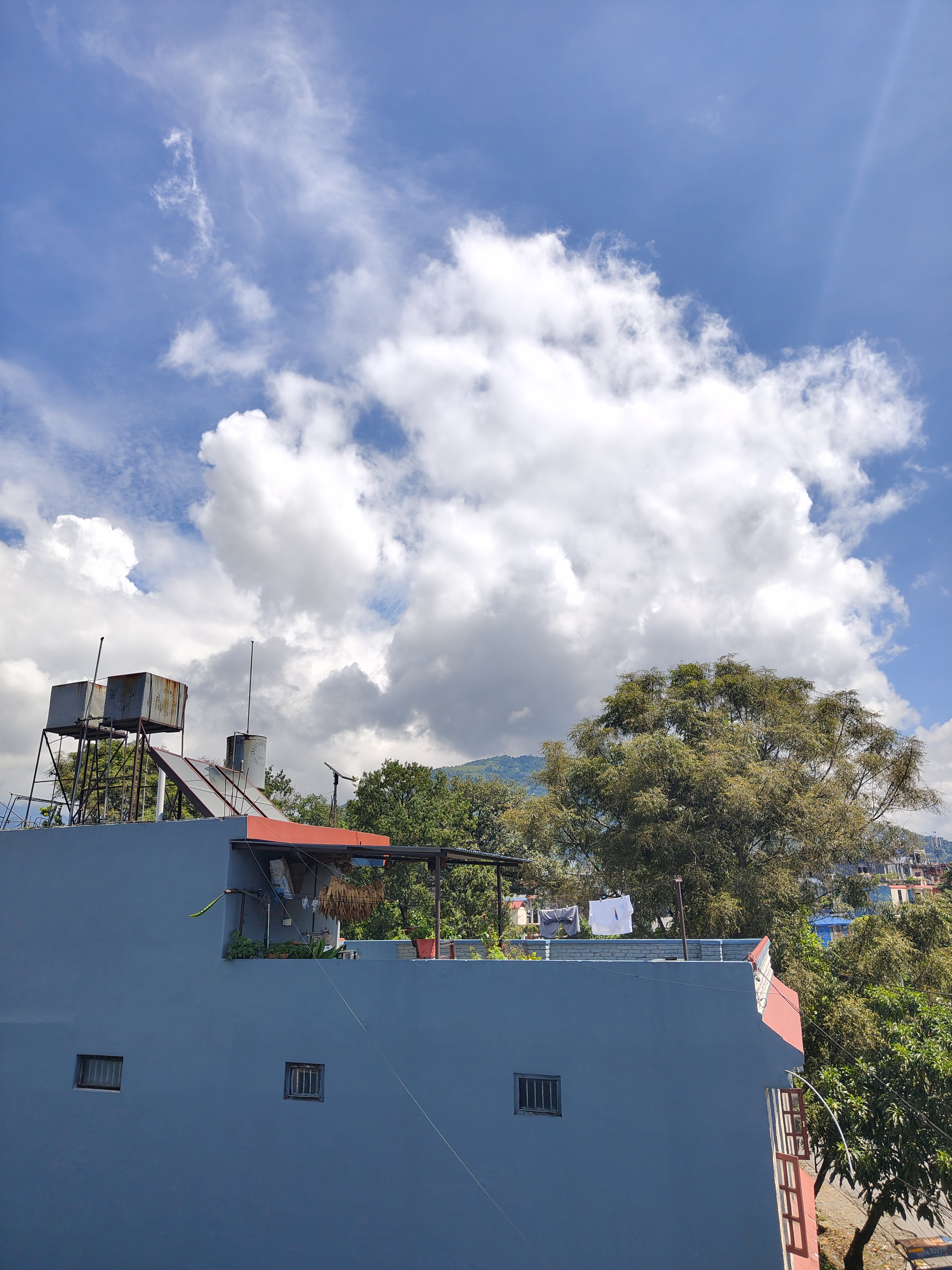 A blue building with a flat roof is in the foreground, featuring a small overhang with plants and clothes hanging to dry.