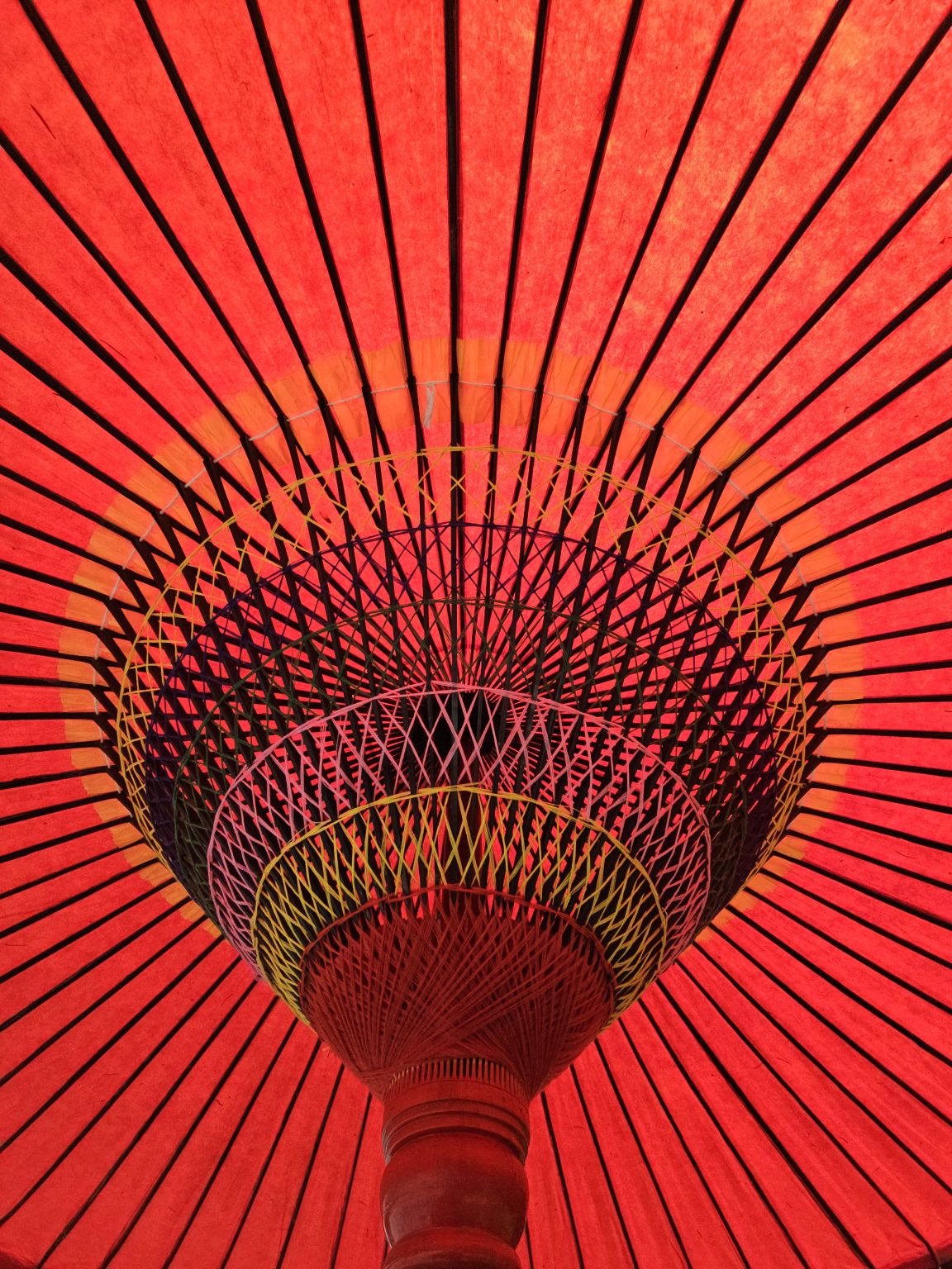 Looking up at the center of a bright red Japanese umbrella with black spokes and detailed weaving. Taken at Portland Japanese Garden.