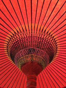 Looking up at the center of a bright red Japanese umbrella with black spokes and detailed weaving. Taken at Portland Japanese Garden.