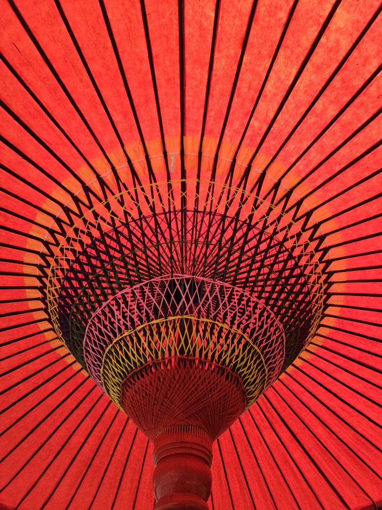 Looking up at the center of a bright red Japanese umbrella with black spokes and detailed weaving. Taken at Portland Japanese Garden.
