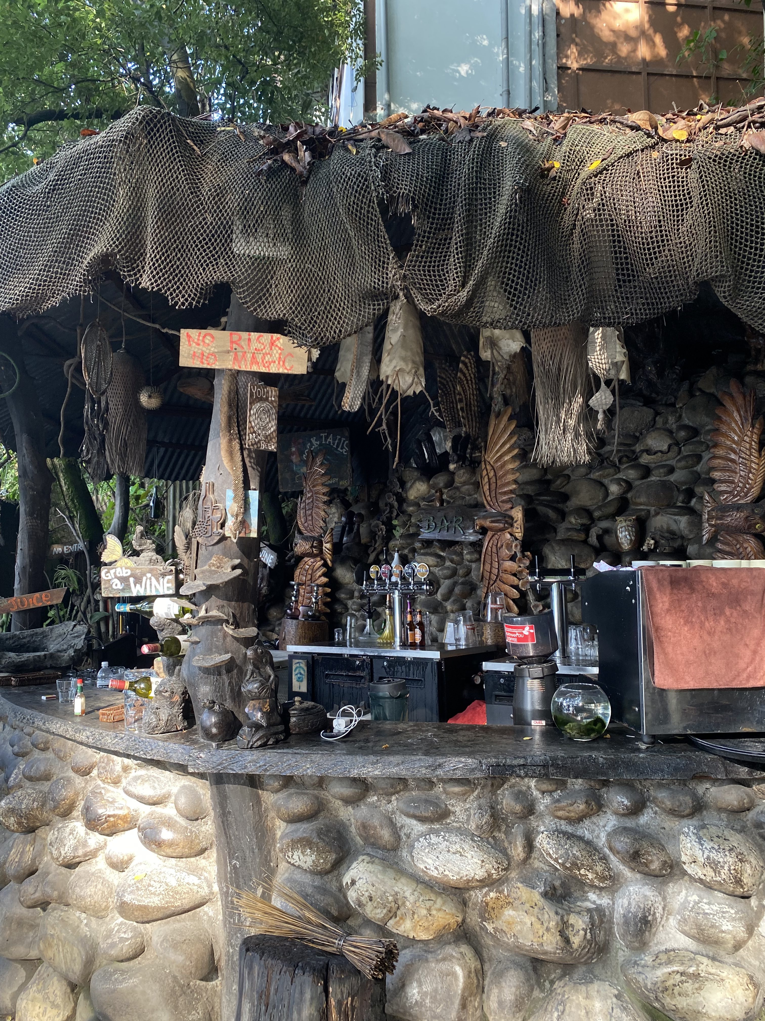 A rustic outdoor bar area featuring a thatched roof adorned with fishing net and various decorative items, including carved wooden figures.