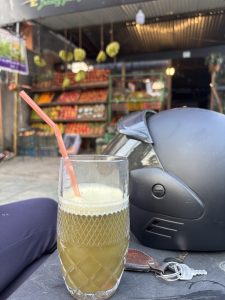 A glass of green juice with a straw sits on a table, partially obscured by a black helmet and a set of keys.
