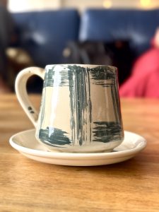 A handmade ceramic coffee mug with a textured green and white design sits on a small matching plate.