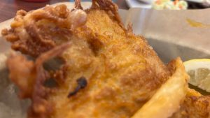 A closeup of some fried fish, a french fry and bit of lemon in the frame.