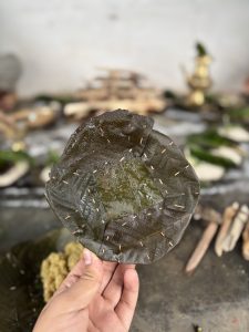 A person holding a large Tapari made from dark green leaves, carefully stitched together with small wooden sticks.