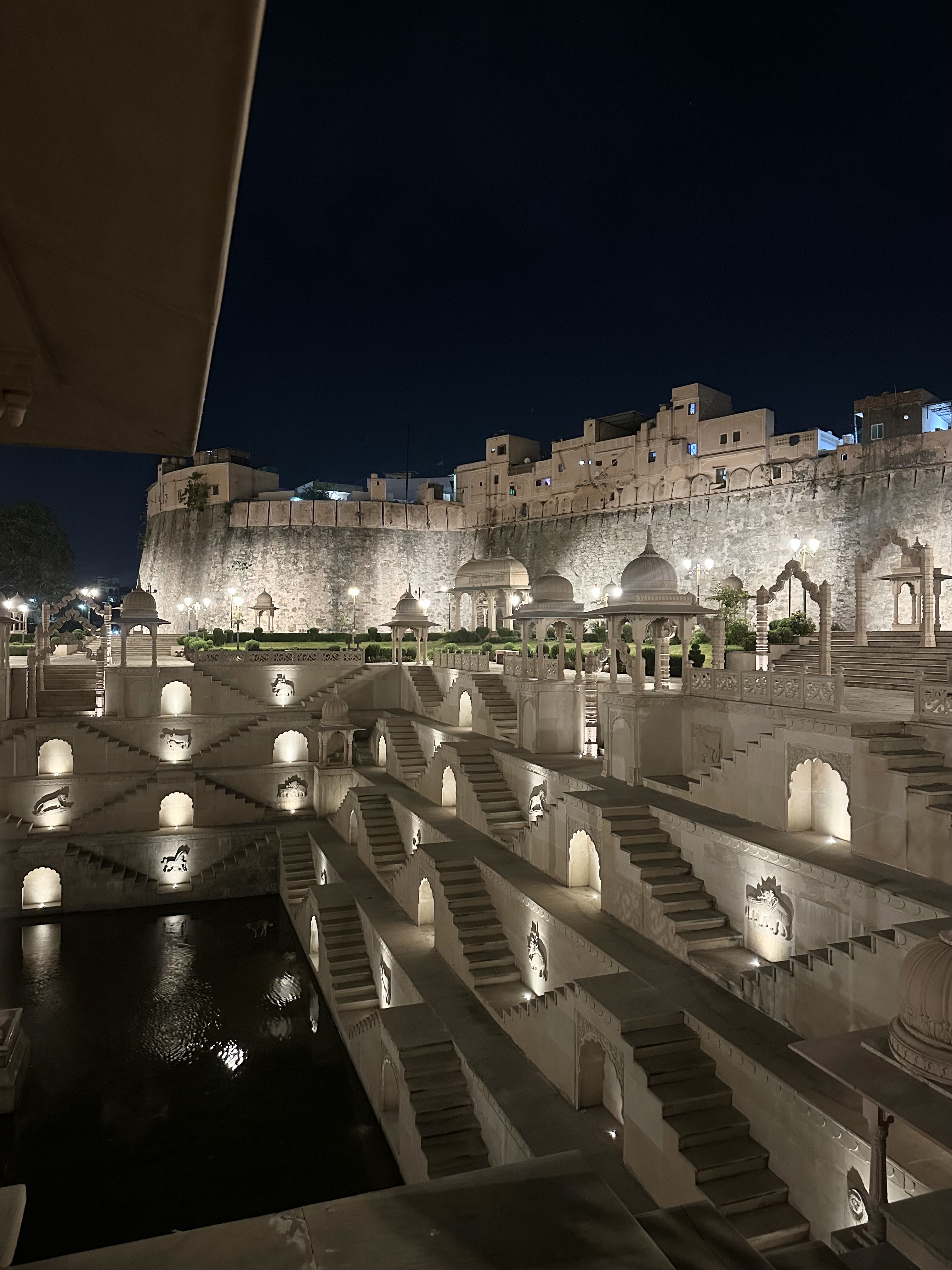 An ancient stepwell in India, highly ornate architecture beautifully lit at night with stone steps, and water at the base.